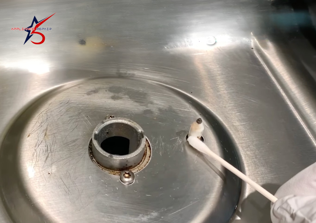 A technician using a cotton swab to carefully clean a ceramic spark igniter on a stainless steel gas cooktop