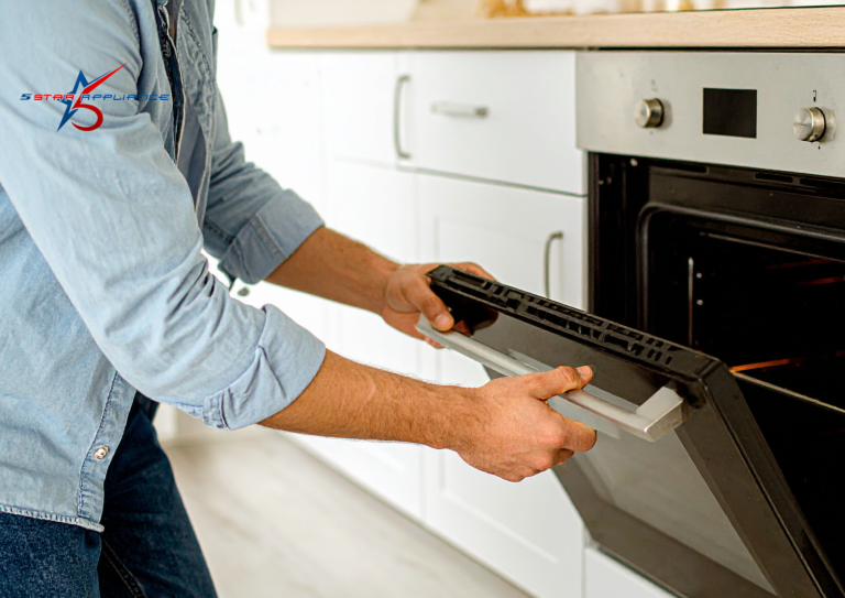 A technician in a denim shirt removing or installing a black glass oven door in a modern white kitchen.